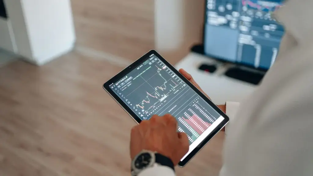 Hand tippt auf ein Tablet mit Kurschart und Orderbuch für die Eingabe einer Wertpapierorder
