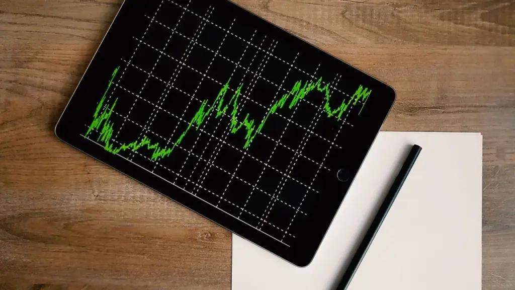 Tablet mit grünem Kursverlauf auf Holztisch als Symbol für Ertragsverwendung bei ETFs