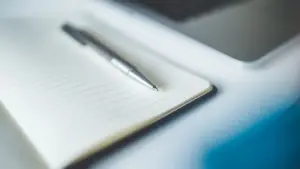 Notizbuch mit Kugelschreiber neben einem Laptop auf einem Schreibtisch